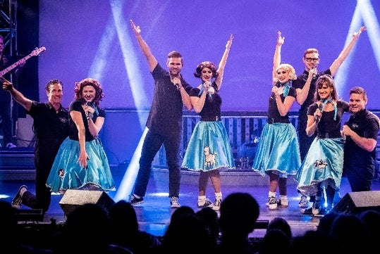 The cast of Hot Rods and High Heels on stage with the women in blue poodle skits and the men in black in Branson, Missouri.