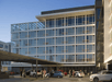 The front glass exterior of the Hotel Eastlund with several cars parked and people walking around on a sunny day.
