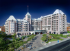Large hotel building with a distinctive architectural design, featuring turrets and archways, surrounded by landscaped gardens and pathways under a clear blue sky.