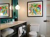 Modern bathroom with a white countertop, sink, towels, toilet, and a colorful abstract tree painting on the wall above the toilet.