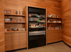 A small market area with built in warm brown shelving full of stands with a black refrigerator case in the middle.