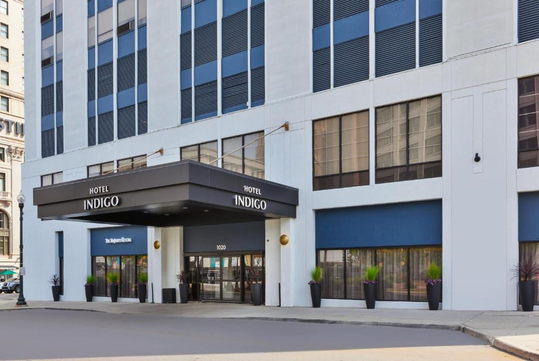 Exterior view of Hotel Indigo entrance with signage above the doorway, featuring large windows and planters on either side of the doors.
