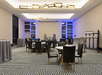 A modern conference room with patterned carpet, multiple round tables, black chairs, and geometric ceiling lights. The walls have a blue accent lighting.