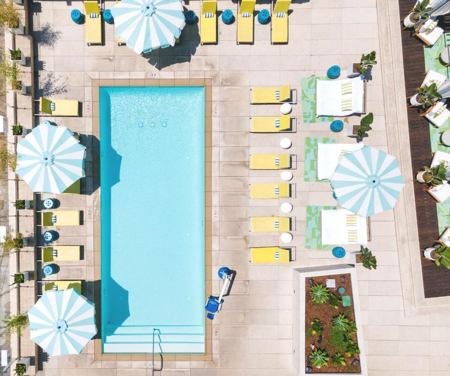 Aerial view of a rectangular swimming pool surrounded by yellow lounge chairs, with blue and white striped umbrellas, and small tables nearby.
