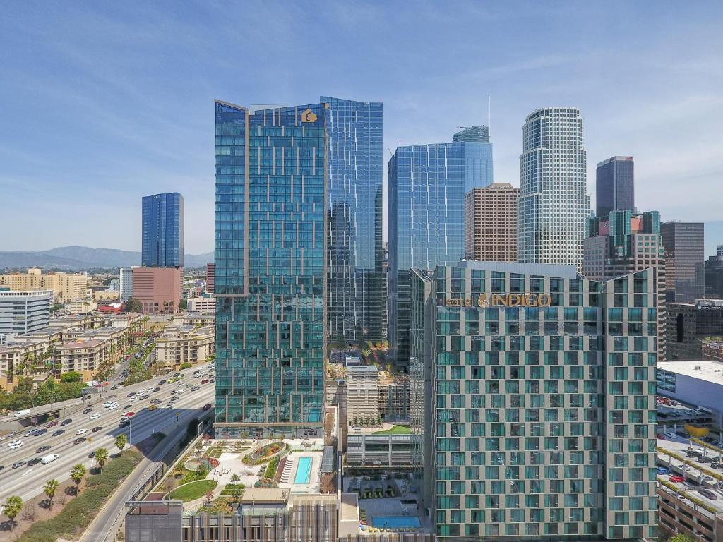 Aerial view of skyscrapers in downtown Los Angeles, featuring glass facades, a rooftop pool, and bustling streets below under a clear blue sky.