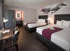 Two queen beds and a well-lit work desk inside a guest room.