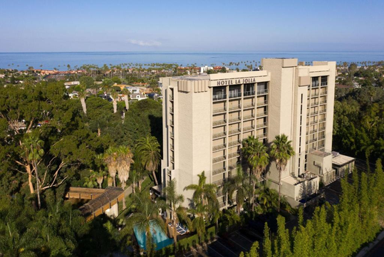 High-rise hotel surrounded by trees with ocean view in the background.