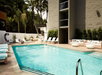 Outdoor swimming pool area with lounge chairs and a modern building backdrop. Palm trees and greenery surround the space, creating a relaxing atmosphere.