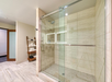 Modern bathroom with a glass-enclosed shower, beige tile walls and floor, and a wooden shelving unit stocked with towels.