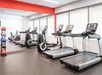 A modern fitness center with a row of cardio equipment in front of large windows and a mirror wall to its left at the Hotel Vance in Portland.