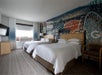 Two double beds with plush bedding and artistic wallpaper inside a guest room.