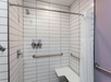 Accessible shower with white tiles, a showerhead, grab bars, soap dispensers, a curtain, and a foldable bench seat.