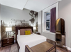 A bedroom with a bed, nightstands with lamps, a standing mirror, and a large wall mural of a vintage amusement park.