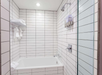 White-tiled bathroom with a showerhead, a bathtub, soap dispensers, and towels on a wall rack.
