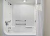 White bathtub with a showerhead, grab bars on three walls, a faucet, and a partially open white shower curtain under a ceiling light.