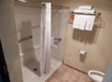 Accessible hotel bathroom with a walk-in shower, white curtain, grab bars, folded towels on a rack, and a toilet with a paper roll.