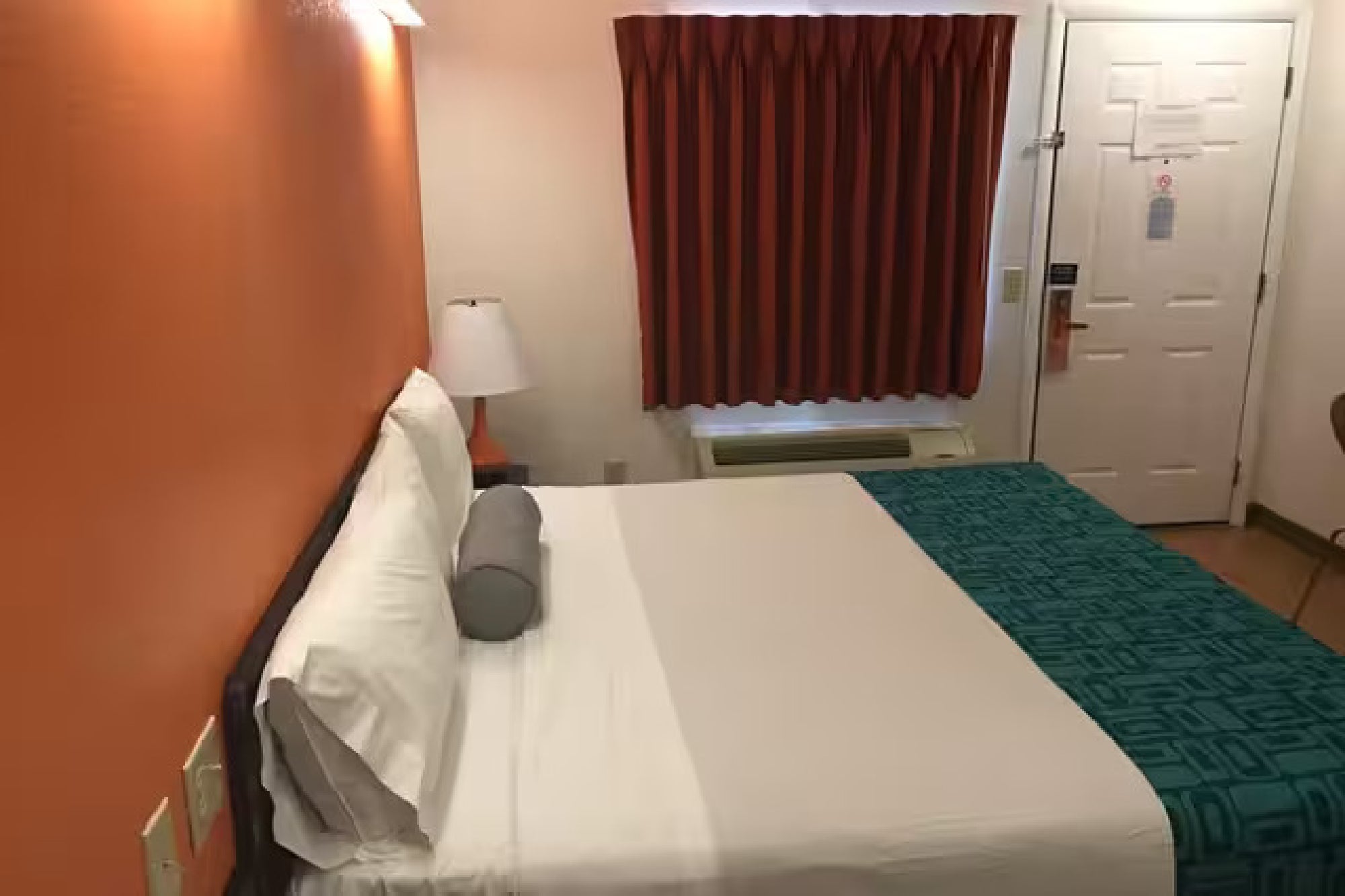 Standard guest room featuring an orange accent wall and a teal patterned bed runner