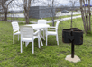 An outdoor picnic area with a white plastic table and chairs next to a small barbecue at Howard Johnson by Wyndham New Braunfels.