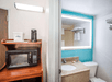 Hotel room showing a kitchenette with a microwave and coffee maker, adjacent to a bathroom with a sink, toilet, and illuminated mirror.