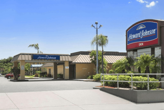 Howard Johnson Inn building with a driveway, tropical plants, and signage. Clear blue sky in the background.