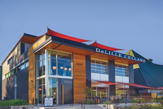 Modern building with wooden accents and red canopies labeled "DeLille Cellars." Large windows and landscaping visible in front.