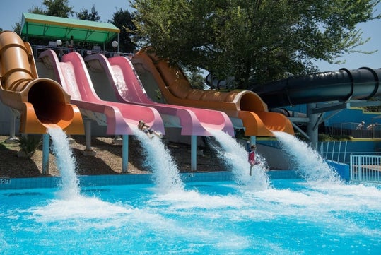 People sliding down colorful water slides into a pool at a water park on a sunny day.