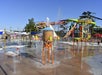 Children play in a water park with colorful water structures and slides under a clear blue sky.