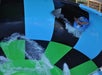 Person in a blue inflatable tube on a colorful water slide with flowing water, featuring blue, black, and green sections.