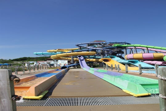 Colorful water slides at an outdoor water park, with clear blue skies above and splash lanes extending below.
