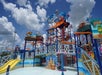 Colorful water park with slides, play structures, and water sprayers under a partly cloudy sky. Children are playing, and a sign reads "Beach Time.