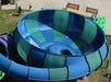 Aerial view of a water slide funnel with blue and green sections and flowing water. Tubes and a deck are visible nearby.