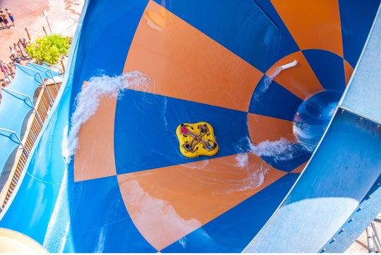 Aerial view of four people in a yellow tube riding down a large orange and blue checkered waterslide.