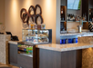Modern hotel bar with a display case of snacks and drinks, a countertop, artistic wall decor, and a TV.