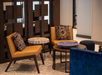 Modern lounge area with brown chairs, patterned cushions, round tables, and blue accents.