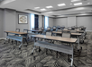 Conference room with rows of rectangular tables and chairs arranged classroom style, patterned carpet, large windows, and modern decor.