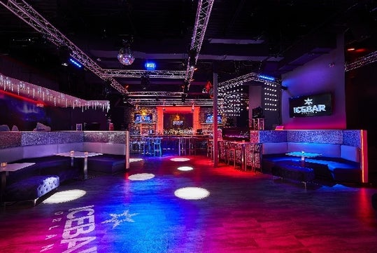 The Fire Lounge, a dark room with red and blue lights shining down, curved booths with tables at them, and a bar on the far wall.