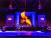 Bartender performs a fire-breathing trick behind an illuminated bar, surrounded by bottles and two "FIRE" signs on either side.