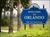 Blue sign reads, "Welcome to Orlando, The City Beautiful," surrounded by greenery and trees.