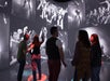 Four people stand inside a room with walls covered in large black-and-white concert photographs, observing the immersive display.
