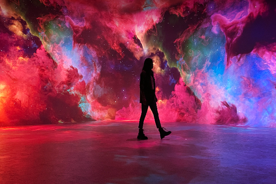 A person walks across a floor in front of a vivid, colorful cosmic background resembling a nebula.