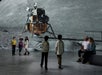 Several children and two adults observe a large screen displaying a lunar lander on the moon's surface in an indoor exhibition space.