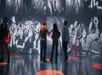 Three people stand in a room surrounded by large black-and-white concert photos.