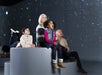 Four people, including two children and two older adults, sit on a round platform indoors, looking up at a projected starry night sky.