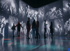People standing and talking in an art gallery with large black-and-white concert photographs projected on the walls.