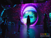 People standing in front of a large LED screen displaying a colorful, abstract eye design in a dark exhibition space.