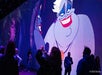 People stand in a dark room facing a large wall projection of Ursula from Disney's "The Little Mermaid." The © 2023 Disney copyright is visible in the corner.