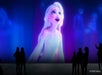 A large screen displays an animated character with white hair, while silhouetted people stand observing in the foreground. © 2023 Disney.