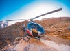 Maverick Airbus helicopter parked on a flat red rock area with several rock formations behind it with the sun shining over it.