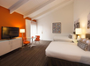 2 Queen beds, a flat-screen TV, and a table and chair for 2 inside a guest room.
