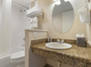 Bathroom with a granite countertop sink, oval mirror, and tissues on the right. Towels are stacked on a rack above a white bathtub with a shower curtain.